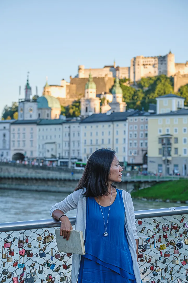 Hyunok Jang auf einer Brücke über die Salzach, dahinter die Salzburger Altstadt und die Festung Hohensalzburg.